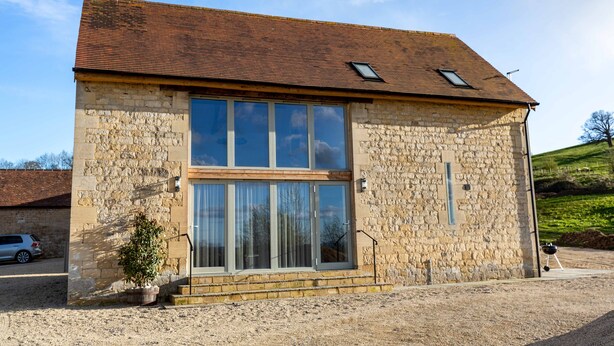 A stone building with a tiled roof, large windows, and a small garden area. - Luxury 2-Bed Cotswolds Barn with Two Ensuite Kings (Gloucester)