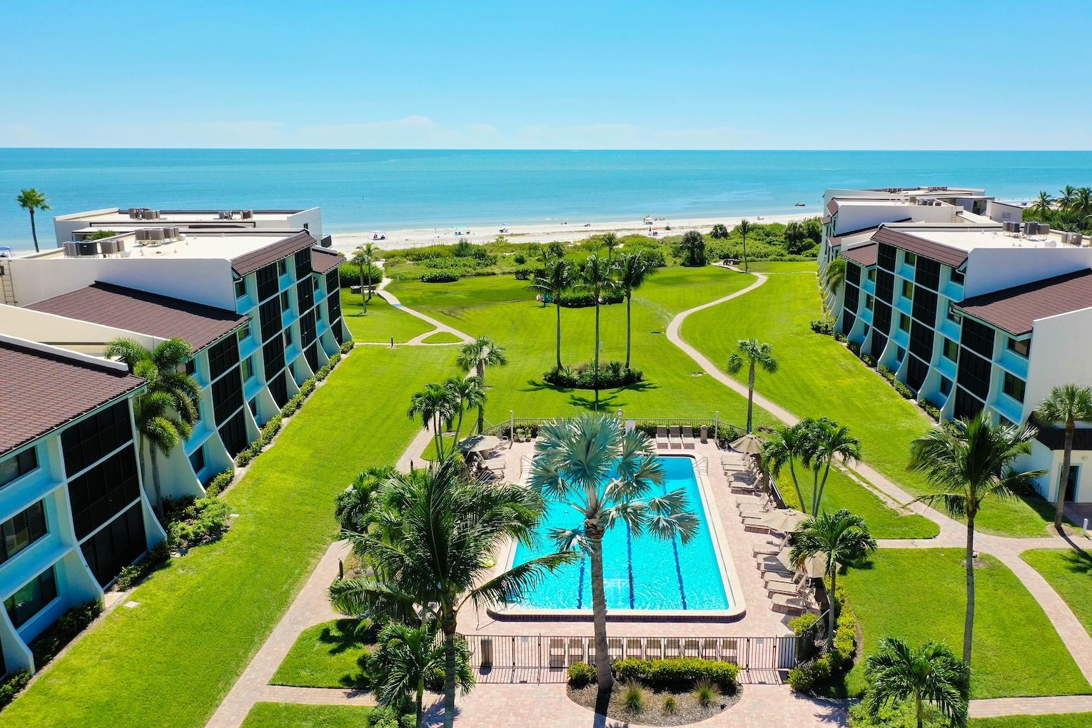 Een resort met een centraal gelegen zwembad, palmbomen en uitzicht op het strand.