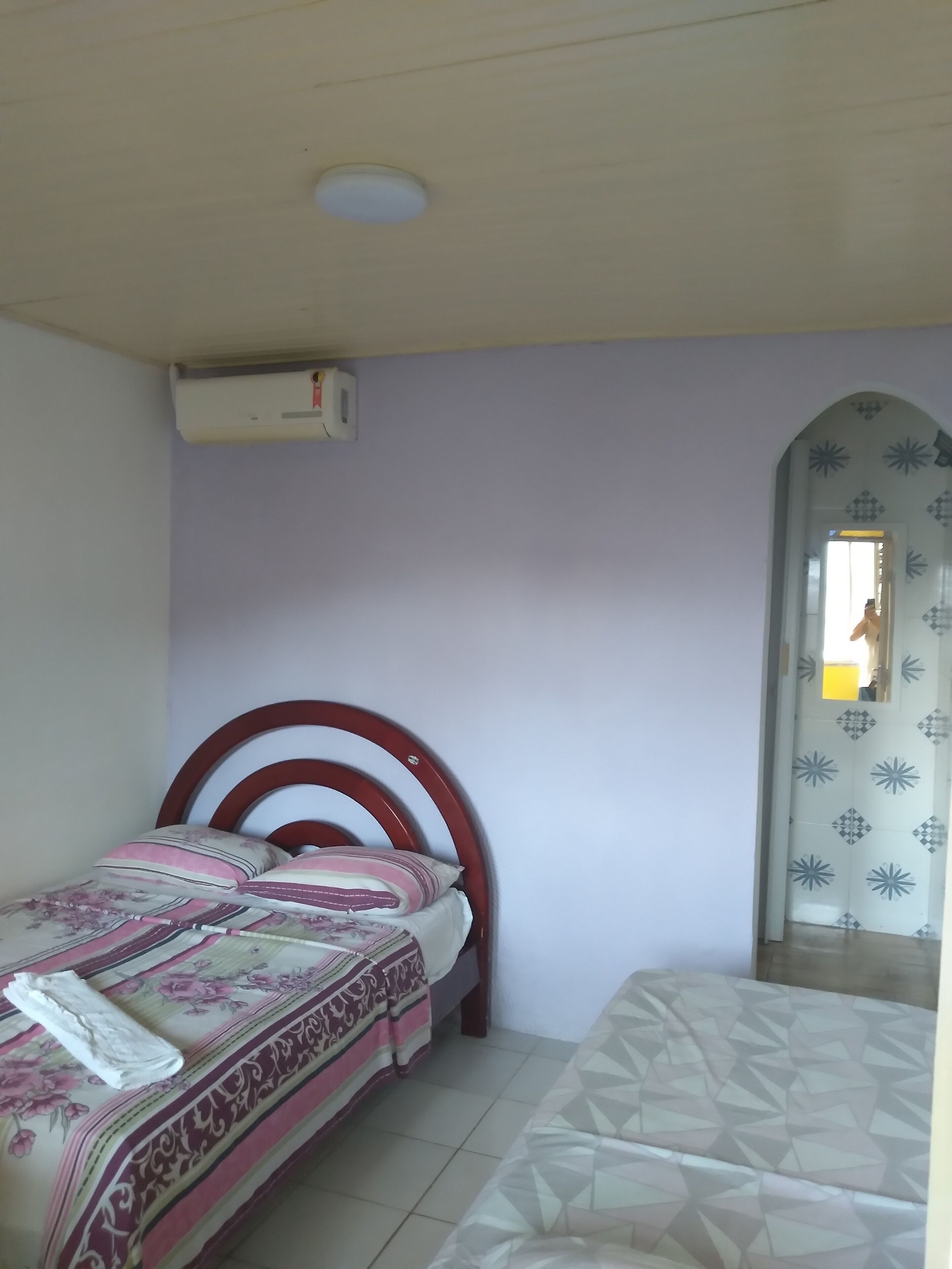 Un dormitorio con una cama individual, cabecera de madera, aire acondicionado de pared y una puerta con diseños geométricos.