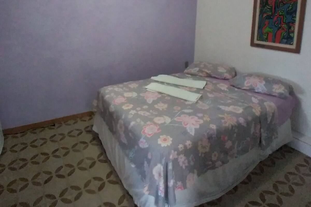 Ein Schlafzimmer mit Bett, einem gemusterten Teppich, einer Deckenleuchte und einem Wandbild.
