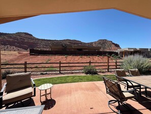 An outdoor patio with a view of a mountainous landscape, a wooden fence, and a building in the background. - Kanab Retreat Near Zion | Pool, Hot Tub & Views (Kanab)