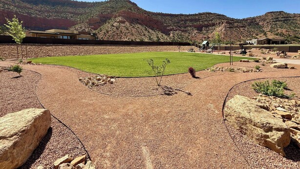 Zona enjardinada amb un camp de gespa, un parc infantil i un edifici amb teulada inclinada.