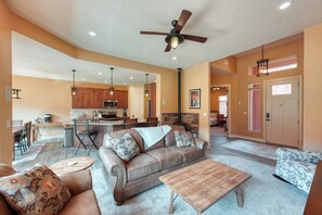 A spacious living room with a sofa, coffee table, and a fireplace. There is a kitchen area with modern appliances and a dining space. - Kanab Retreat Near Zion | Pool, Hot Tub & Views (Kanab)
