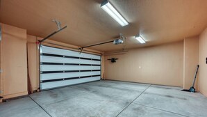 Un garatge amb porta tancada, llums fluorescents al sostre i una escoba recolzada a la paret.