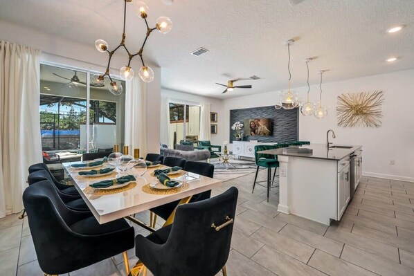 A modern kitchen with a central island, dining area with black chairs, and a ceiling fan. - Relax in Style at this Spacious 4-Bedroom Villa! (Kissimmee)