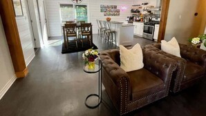 Un salón amplio con un sofá de cuero marrón, una zona de comedor con sillas y una cocina al fondo.