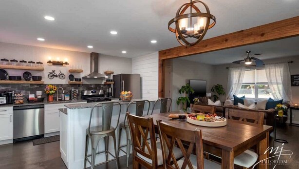 Una cocina moderna con una isla central, electrodomésticos de acero inoxidable y un comedor con sillas de madera y una lámpara de araña.