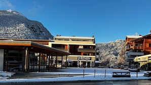Une ville enneigée, avec des bâtiments en bois, un restaurant appelé « Les 2 bouchons » et une montagne en arrière-plan.