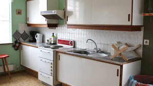 A compact kitchen with white cabinets, a stove, a sink, and a coffee maker. - Old Authentic Icelandic Farmhouse (Laugar)