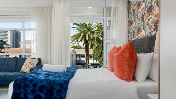 Ein Hotelzimmer mit Bett, Sofa und Balkon mit Blick auf Palmen und Gebäude.