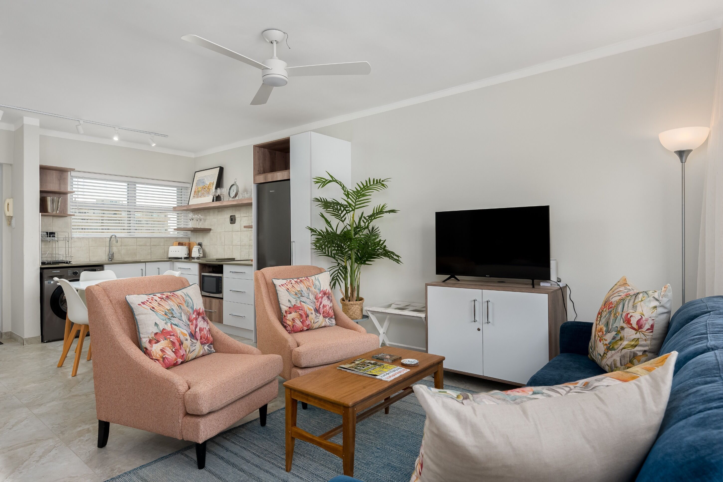 Ein modernes Wohnzimmer mit Sofa, Sesseln, Couchtisch, Fernseher und Deckenventilator.
