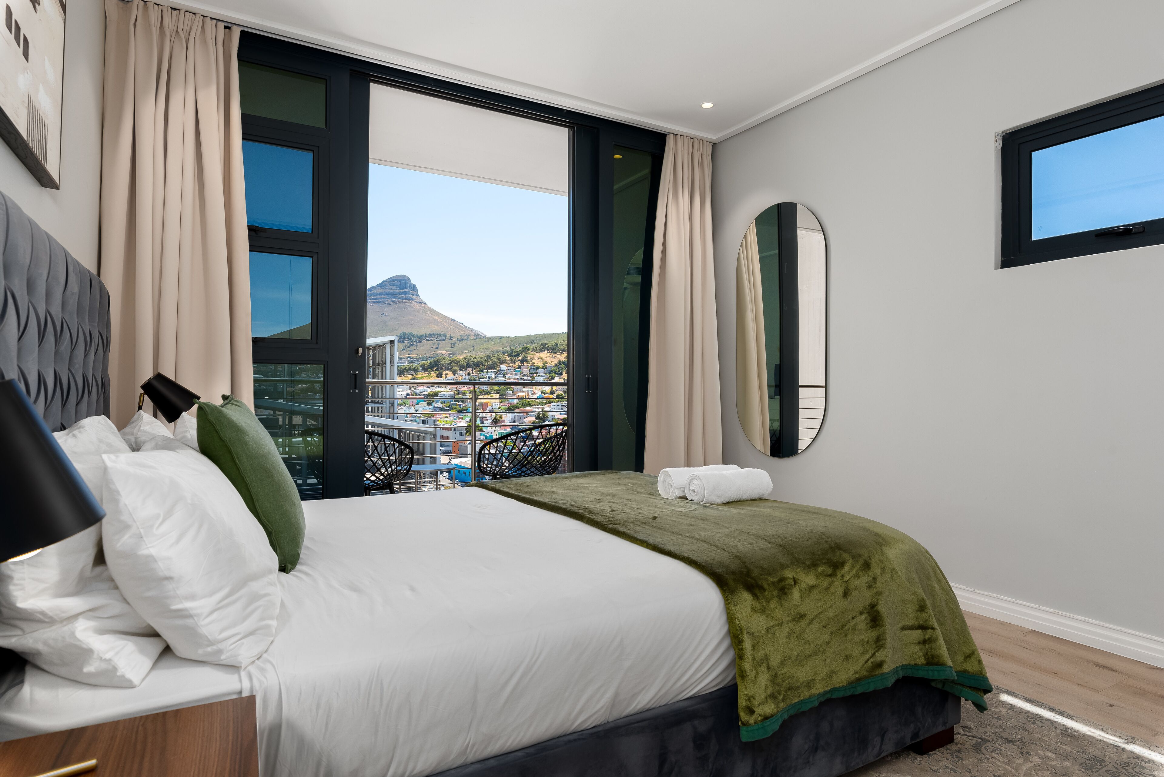 A hotel room with a large bed, a view of a cityscape and a mountain, and a window with curtains.