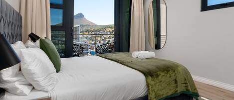 A hotel room with a large bed, a view of a cityscape and a mountain, and a window with curtains.