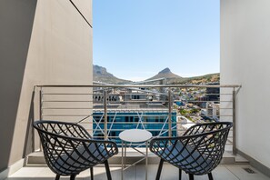 A balcony with two chairs and a small table, overlooking a cityscape with buildings and a mountain. - Spacious 16 on Bree Apartment Balcony Wifi (Cape Town)