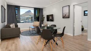 Un salon moderne avec une table en verre, des chaises noires, un canapé gris et une vue sur une montagne.
