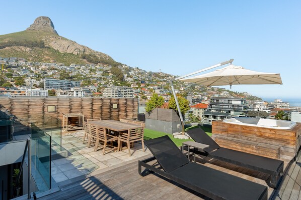 A rooftop terrace with a wooden deck, lounge chairs, a table, and a hot tub.