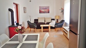 Un espace de vie compact comprenant un canapé, deux fauteuils, une table à manger ornée d’un vase de fleurs, un réfrigérateur et un tableau accroché au mur.