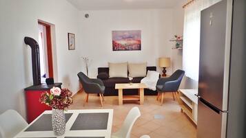 Un espace de vie compact comprenant un canapé, deux fauteuils, une table à manger ornée d’un vase de fleurs, un réfrigérateur et un tableau accroché au mur.