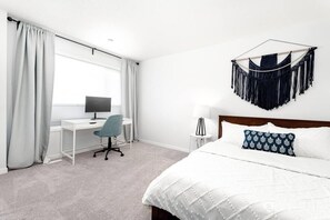 Una camera d'hotel con un letto, una scrivania con un computer, una sedia e un pannello decorativo in macramè.