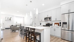 Een moderne keuken met witte kasten, roestvrijstalen apparatuur en een centraal eiland met barkrukken.