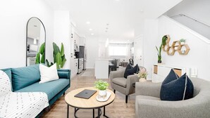 A modern living room with a sofa, armchair, and coffee table, a kitchen in the background, and a staircase leading to an upper level. - Paisley. Sleeps 6. Dog Friendly. A/C (Southwest)