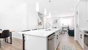 A modern kitchen with white cabinetry, a central island with a sink, and a dining area with a table and chairs. - Paisley. Sleeps 6. Dog Friendly. A/C (Southwest)