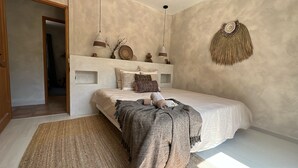 Une chambre à coucher comprenant un lit, un luminaire suspendu, un élément décoratif fixé au mur et une porte donnant sur une autre pièce.