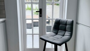A modern room with a black leather chair, a white door with glass panels, and a view of the outside. - Londwell - Chelsea Garden Flat - Private Oasis (London)