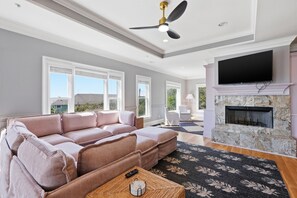 A modern living room with a sectional sofa, a fireplace, a flat-screen TV, and a ceiling fan.