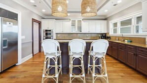A kitchen with white cabinets, a central island with bar stools, stainless steel appliances, and a hanging light fixture. - 4 Bed 5 Bath Luxury Beach Front Home w/Ocean Views (Tybee Island)