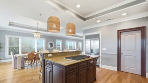 A kitchen with a central island, dark cabinetry, and a dining area with chairs and a table. - 4 Bed 5 Bath Luxury Beach Front Home w/Ocean Views (Tybee Island)