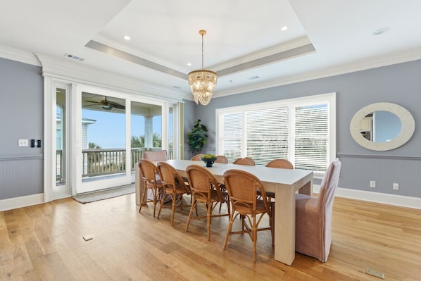 A dining room with a large table, wicker chairs, a chandelier, and a view through the glass doors.