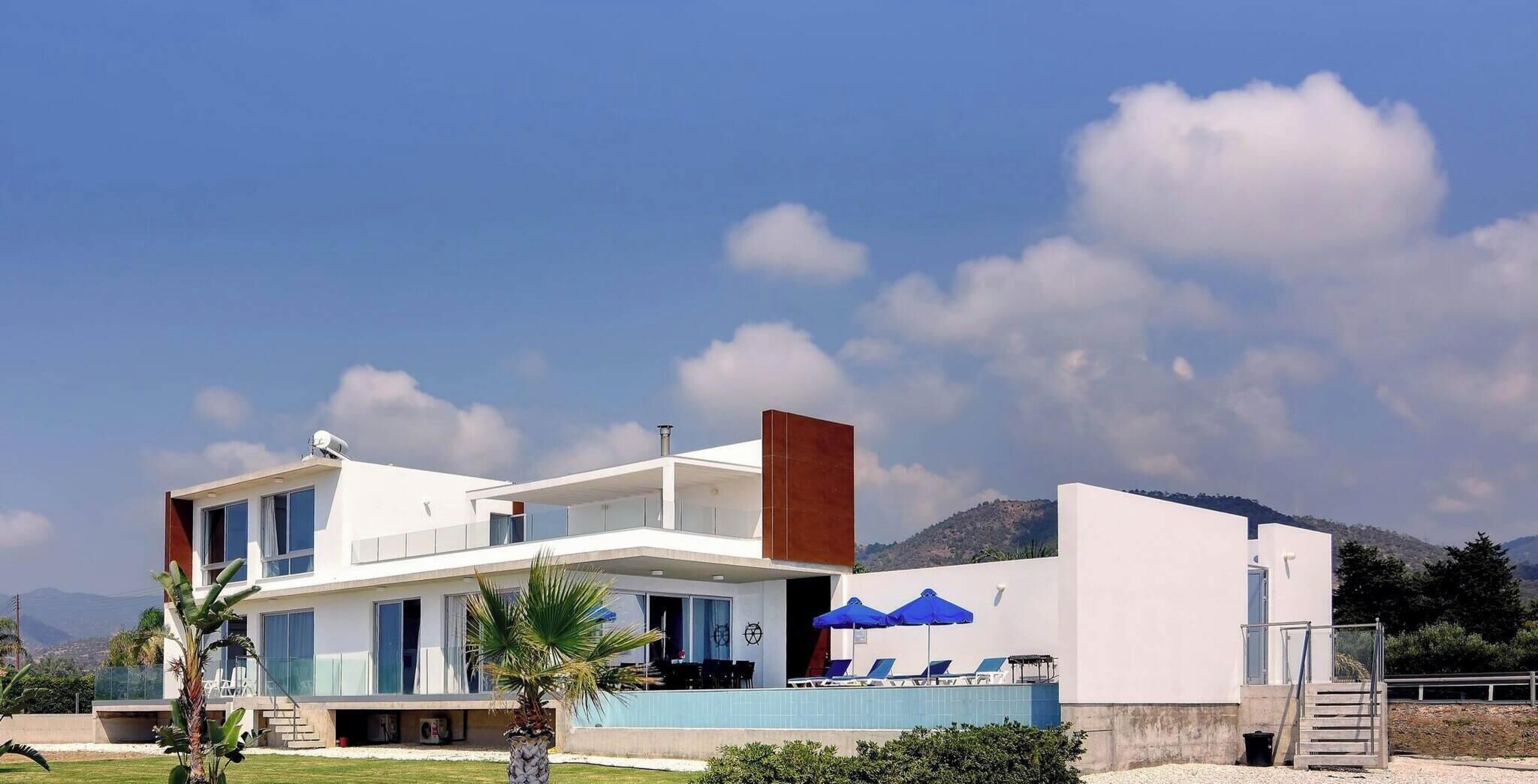 A modern two-story building with a flat roof, large windows, and a visible outdoor seating area with umbrellas.