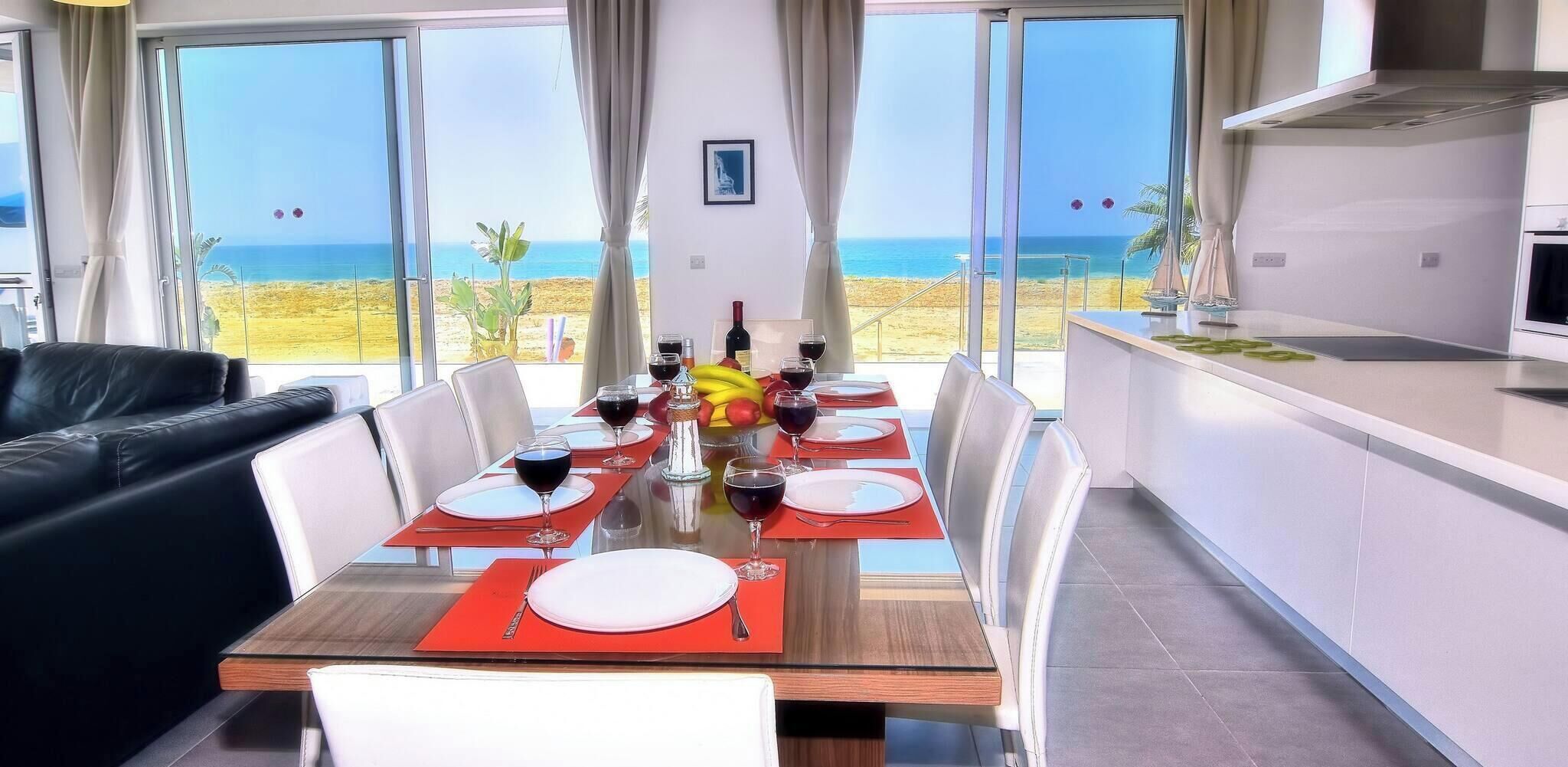 A dining area with a table set for six, a kitchen, and a view of the beach.