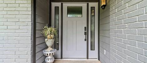 A grey brick exterior with a door, a small white planter with a plant, and a textured concrete step.