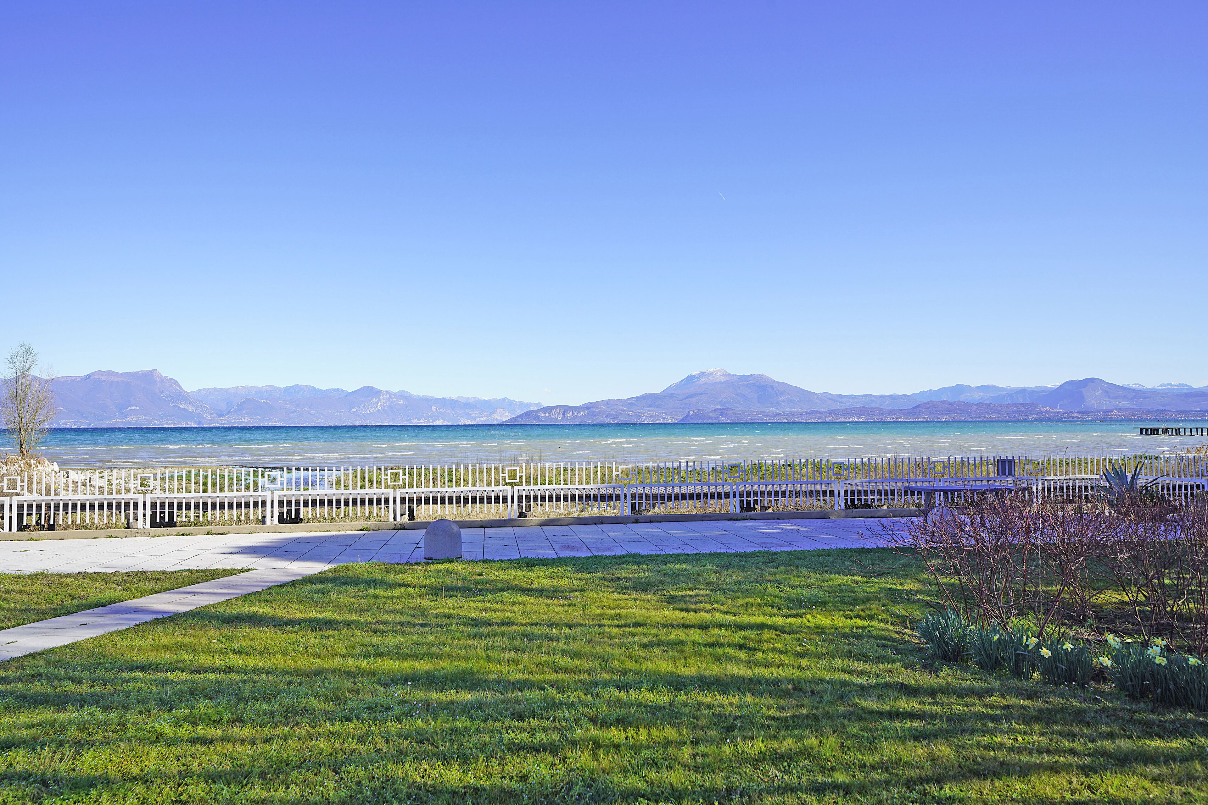 A grassy area with a white fence and a view of a lake and mountains.