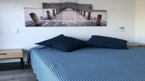 Ein Schlafzimmer mit einem großen Bett, zwei Nachttischen und einem Wandbild, das einen Steg zeigt.