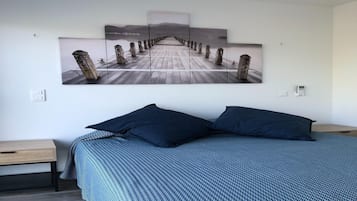 Quarto com uma cama grande, duas mesas de cabeceira e uma obra de arte na parede retratando um cais.