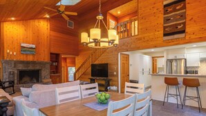A spacious living room with a fireplace, a dining area with a wooden table and chairs, a kitchen with white cabinets, and a staircase leading to an upper level. - RR070 | Updated open concept home close to ranch amenities and hiking trails. (Black Butte Ranch)