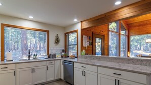 A modern kitchen with white cabinets, a dishwasher, and large windows with blinds. - RR070 | Updated open concept home close to ranch amenities and hiking trails. (Black Butte Ranch)