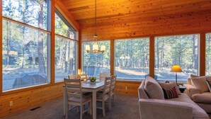 A cozy cabin interior with a dining area, a sofa, and large windows offering a view of the forest. - RR070 | Updated open concept home close to ranch amenities and hiking trails. (Black Butte Ranch)