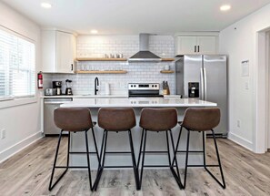 A modern kitchen with white cabinets, a stainless steel refrigerator, a built-in oven, and a central island with bar stools.
