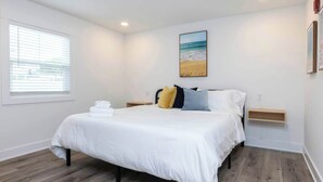 Een slaapkamer met een bed, een raam, een schilderij en een nachtkastje.