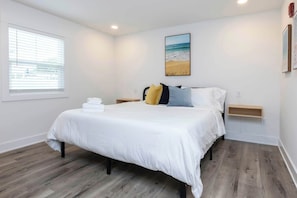 A bedroom with a bed, a window, a painting, and a nightstand.
