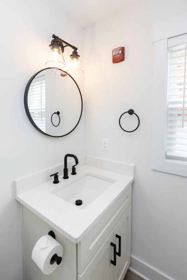 A bathroom with a white sink, black faucet, and a round mirror with lights.