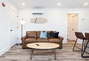 Una sala de estar moderna con un sofá de cuero marrón, una mesa redonda de centro y un adorno de tabla de surf en la pared.