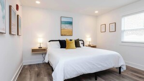 A bedroom with a bed, two bedside tables, a nightstand, a window, and wall-mounted artwork. - Teahupo'o - Loft #2 - 8 min walk to the beach (Virginia Beach)