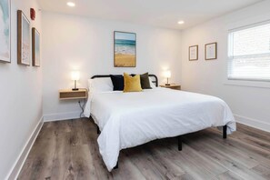 A bedroom with a bed, two bedside tables, a nightstand, a window, and wall-mounted artwork.
