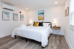Habitación de hotel con cama, mesitas de noche, aire acondicionado instalado en la pared, obra de arte enmarcada y ventana.