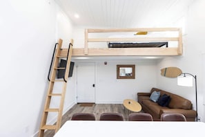 A compact room with a bunk bed, a desk, a chair, a sofa, and a lamp. - Jeffreys Bay - Loft #3 - 8 min walk to beach (Virginia Beach)